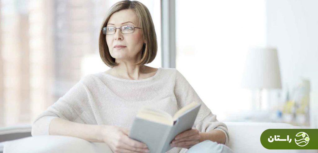 زنی میانسال در سن یائسگی که در کتاب خواندن و نگاه کردن به بیرون از پنجره است
