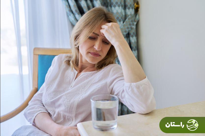 زنی در سن یائسگی که روی صندلی نشسته و به لیوان آب روی میز خیره شده است