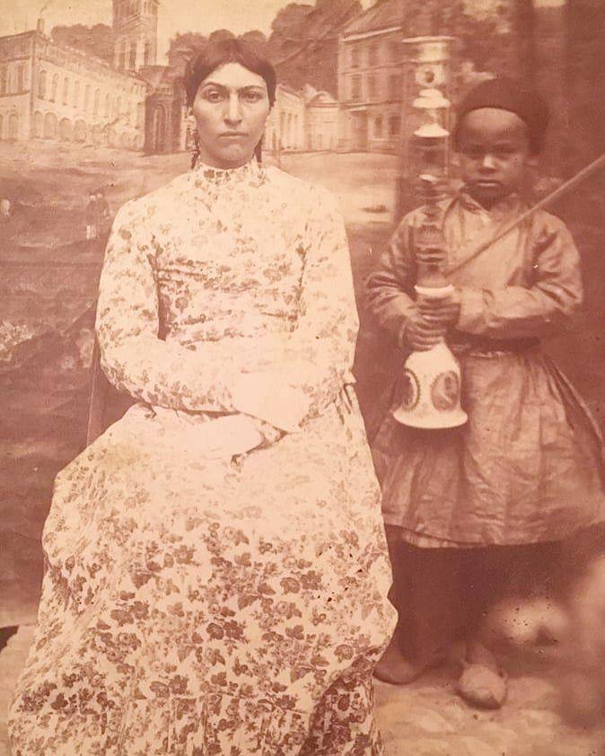 (عکس) یک شاهزاده خانم قجری سال ۱۲۹۴ تهران در کنار خدمتکار قلیان به دست در آتلیه عکاسی